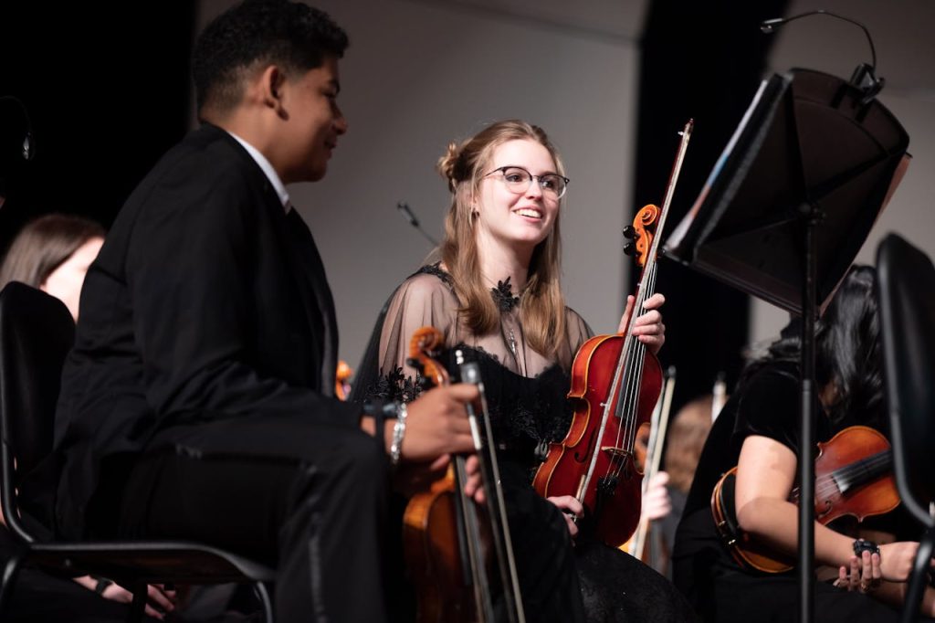 Young musicians in formal attire performing with violins in an orchestra setting.